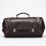 Dark Brown leather duffel bag against a dark brick wall.