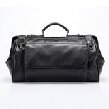 Black leather duffel bag on a dark surface with a brick wall background